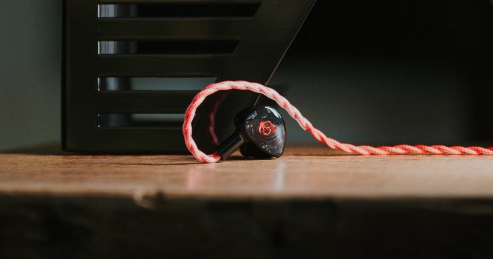 single fatfreq x hbb deuce earphone with attached cable running across butcher block table