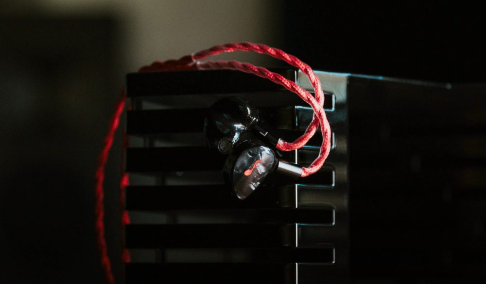 fatfreq x hbb deuce earphones with attached red blood cable hanging over corner of amp dark