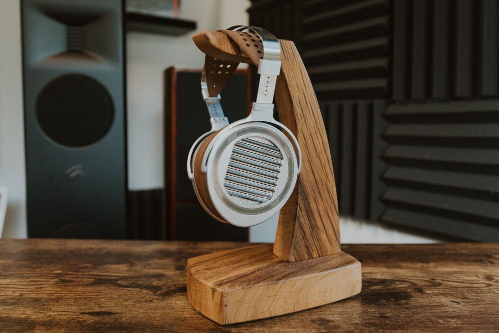 HiFiMAN Susvara Unveiled profile on wooden headphone stand with speakers in background