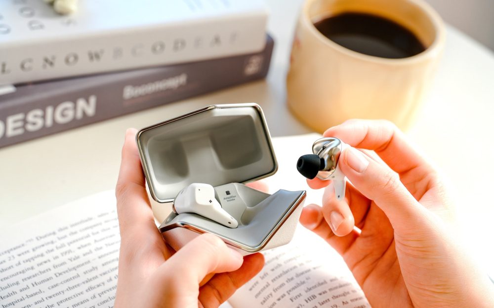 Human holding HiFiMAN Svanar Wireless Jr case and single earbud with coffee and books