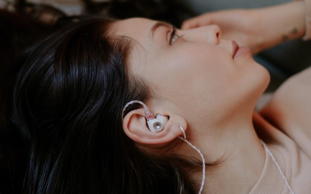 human with dark flowing hair lying down while wearing Meze Alba earphone with attached stock cable