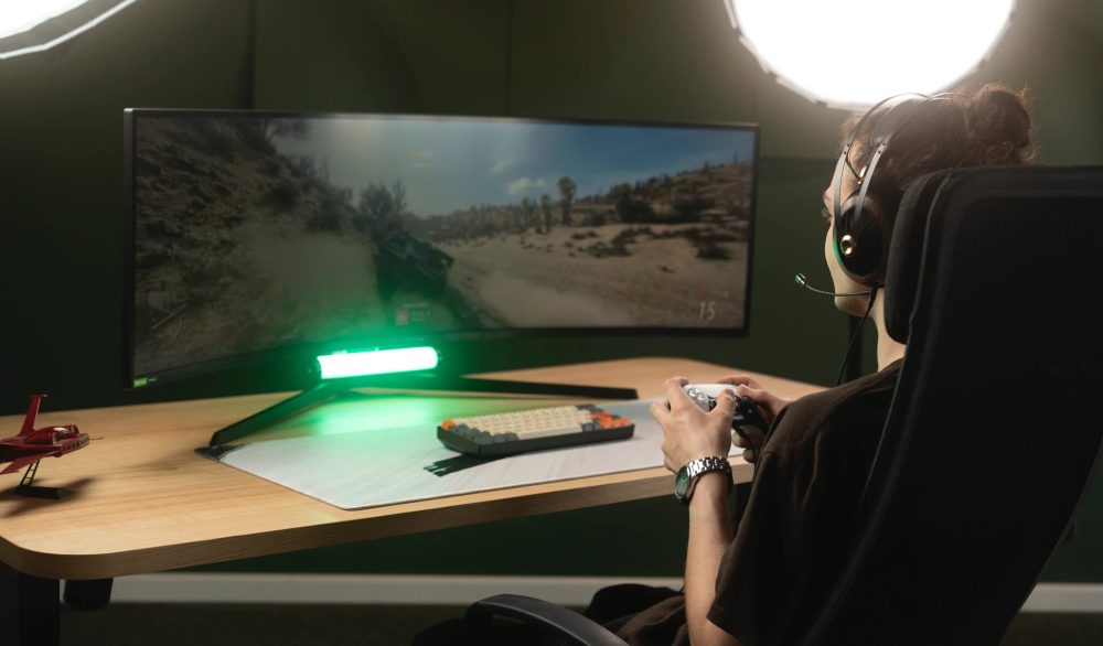 human in gaming chair holding controller wearing Meze headphones in front of widescreen display with green LED